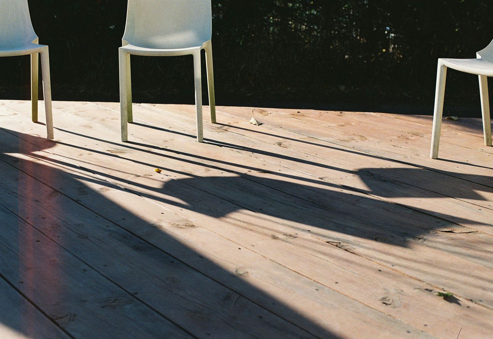 Sunlit deck boards with outdoor chairs casting long shadows