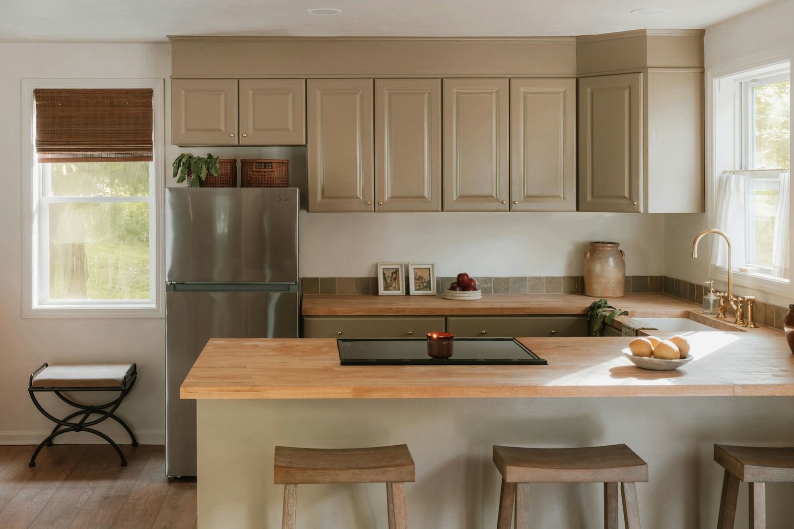 Kitchen with a butcher-block island, wooden stools and cream raised-panel cabinets
