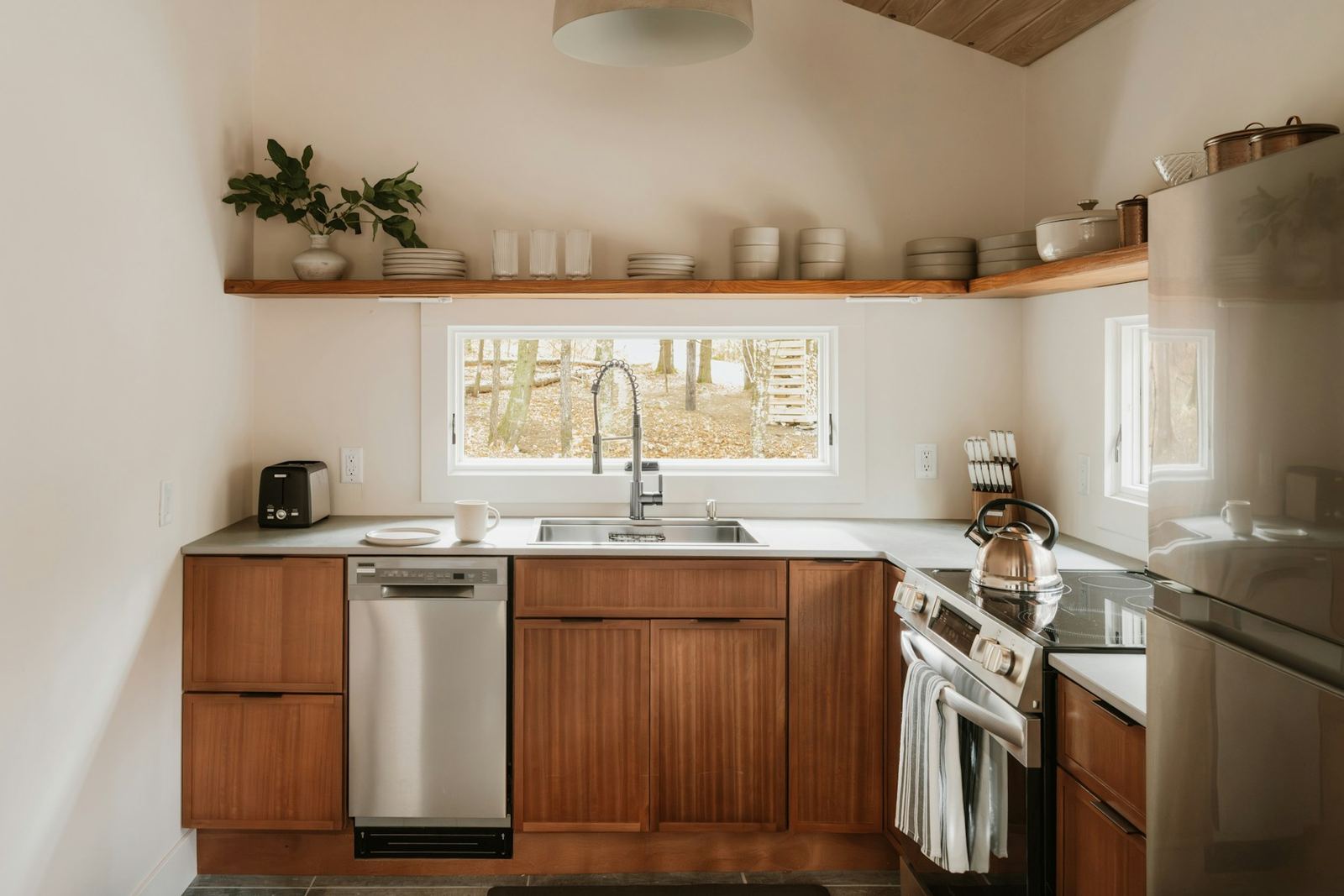 Compact kitchen with walnut lower cabinets, open wood shelving and a window over the sink